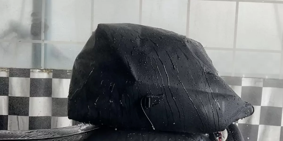 一個覆蓋有光滑深色 PVC 織物的物體在雨中閃閃發光,放置在格子圖案背景前。.